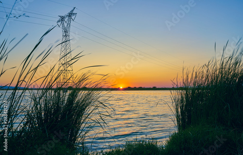 Fototapeta Naklejka Na Ścianę i Meble -  Sunset in a landscape with lake, trees and light towers. Extremadura. Spain