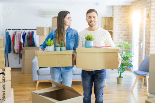 Young couple moving to a new home, smiling happy holding cardboard boxes at new apartment