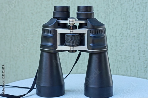 one big black binoculars stands on a white table on a gray background