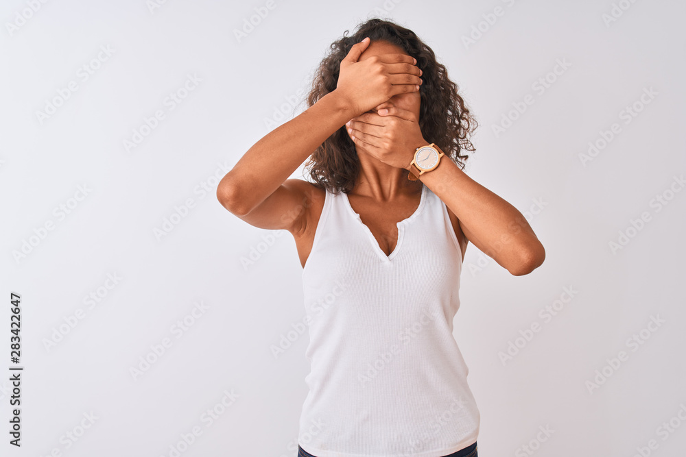 Young brazilian woman wearing casual t-shirt standing over isolated white background Covering eyes and mouth with hands, surprised and shocked. Hiding emotion