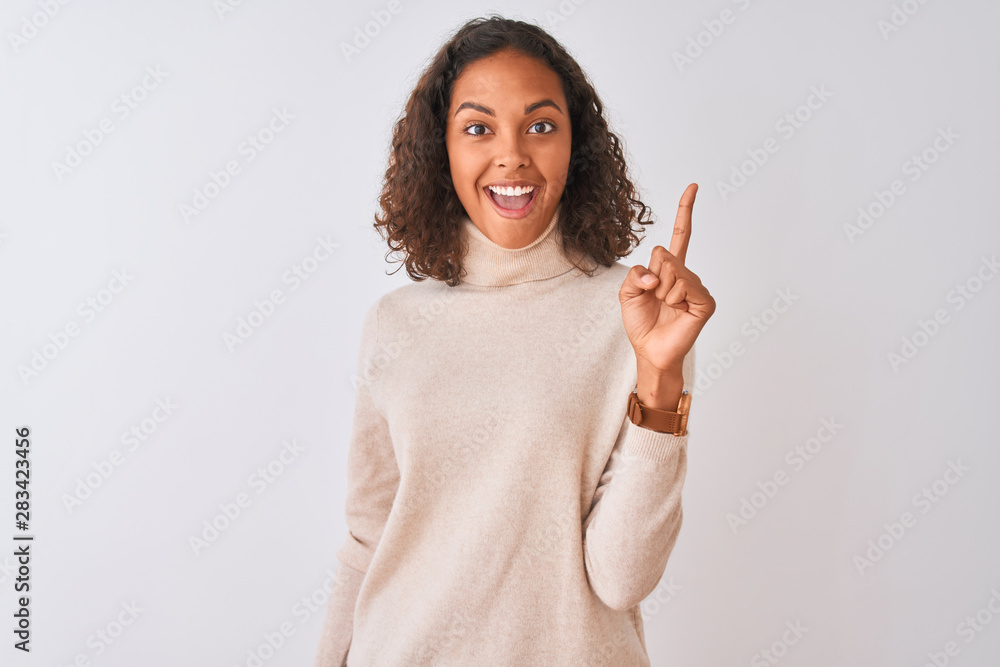 Young brazilian woman wearing turtleneck sweater standing over isolated white background pointing finger up with successful idea. Exited and happy. Number one. Young brazilian woman wearing turtleneck sweater standing over isolated white background pointing finger up with successful idea. Exited and happy. Number one.