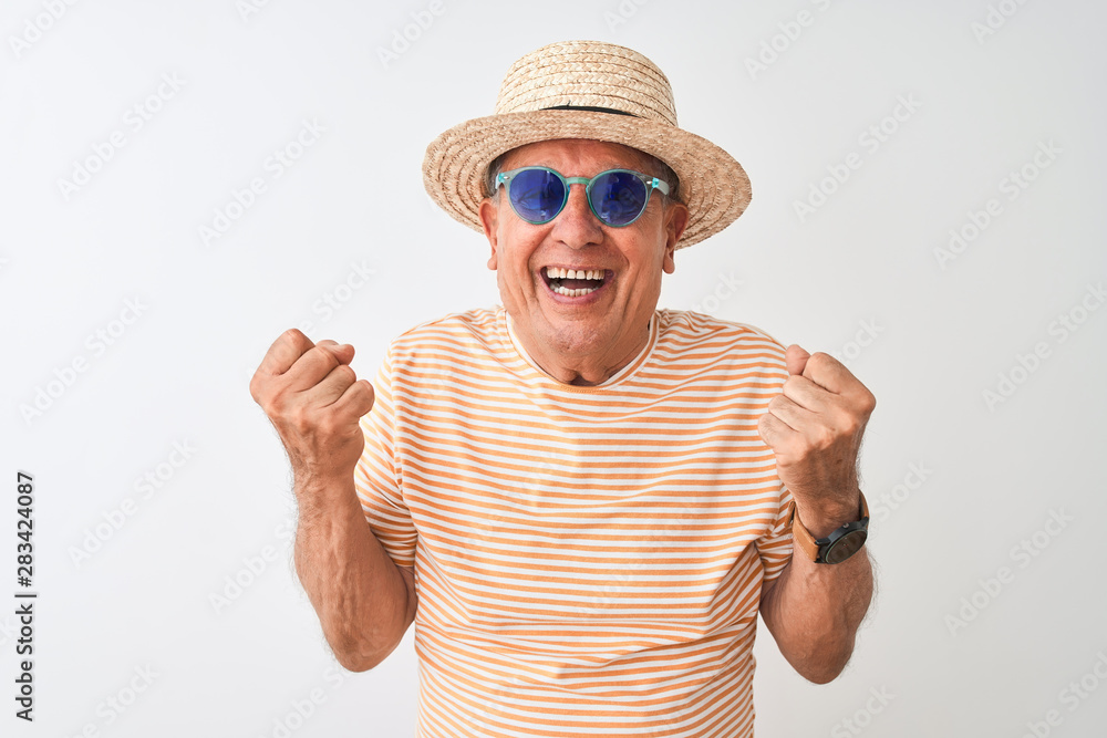 Naklejka premium Senior man wearing striped t-shirt sunglasses and sumer hat over isolated white background screaming proud and celebrating victory and success very excited, cheering emotion