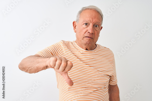 Senior grey-haired man wearing striped t-shirt standing over isolated white background looking unhappy and angry showing rejection and negative with thumbs down gesture. Bad expression.