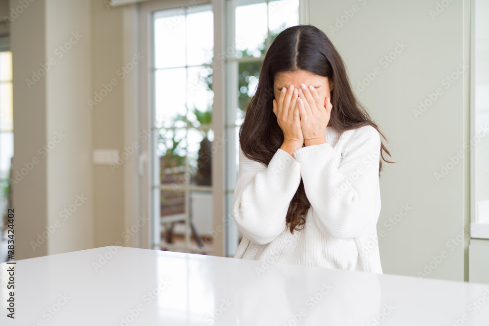 Young beautiful woman at home on white table with sad expression covering face with hands while crying. Depression concept. Young beautiful woman at home on white table with sad expression covering face with hands while crying. Depression concept.