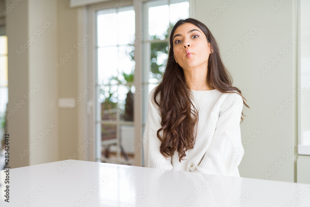 Young beautiful woman at home on white table making fish face with lips, crazy and comical gesture. Funny expression. Young beautiful woman at home on white table making fish face with lips, crazy and comical gesture. Funny expression.
