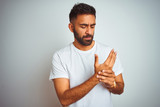 Young indian man wearing t-shirt standing over isolated white background Suffering pain on hands and fingers, arthritis inflammation