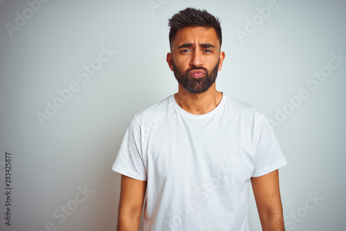 Young indian man wearing t-shirt standing over isolated white background looking at the camera blowing a kiss on air being lovely and sexy. Love expression.