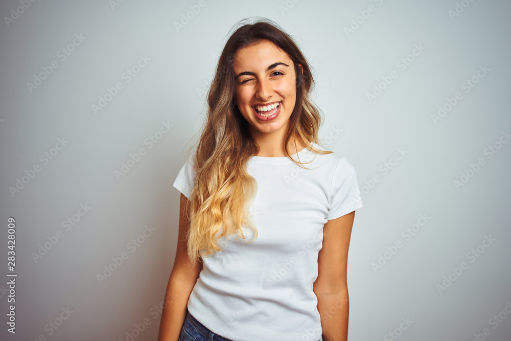 Young beautiful woman wearing casual white t-shirt over isolated background winking looking at the camera with sexy expression, cheerful and happy face. Young beautiful woman wearing casual white t-shirt over isolated background winking looking at the camera with sexy expression, cheerful and happy face.