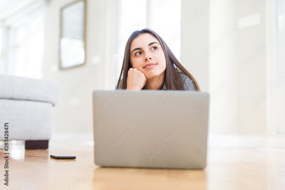 Beautiful young woman laying on the floor using laptop serious face thinking about question, very confused idea Beautiful young woman laying on the floor using laptop serious face thinking about question, very confused idea