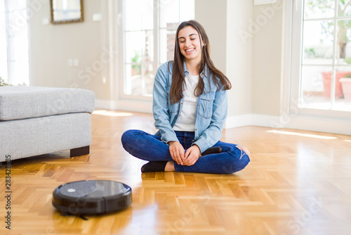 Young woman using automatic vacuum cleaner to clean the floor, controling machine housework robot © Krakenimages.com