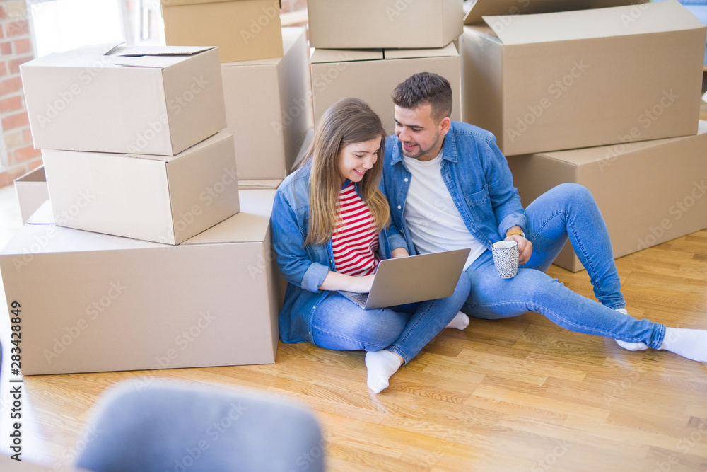Young couple sitting on the floor around cardboard boxes using computer laptop, very happy moving to a new house Young couple sitting on the floor around cardboard boxes using computer laptop, very happy moving to a new house