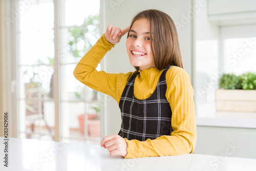 Young beautiful blonde kid girl wearing casual yellow sweater at home Smiling pointing to head with one finger  great idea or thought  good memory