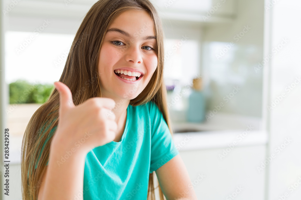 Beautiful young girl kid wearing green t-shirt doing happy thumbs up gesture with hand. Approving expression looking at the camera showing success.