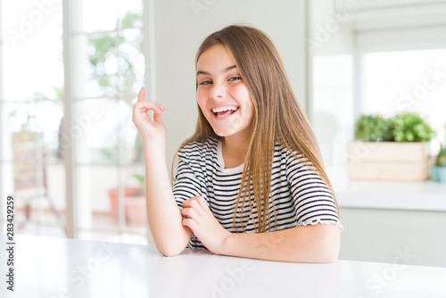 Beautiful young girl kid wearing stripes t-shirt with a big smile on face, pointing with hand and finger to the side looking at the camera.