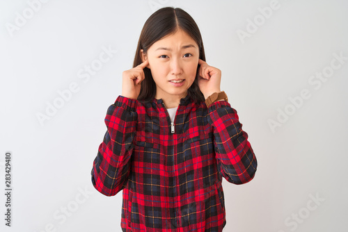 Young chinese woman wearing casual jacket standing over isolated white background covering ears with fingers with annoyed expression for the noise of loud music. Deaf concept. © Krakenimages.com