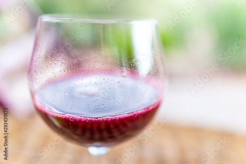 Macro closeup of glass of red pink purple wine or cranberry juice isolated with blurry background in garden