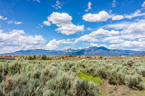 View of Taos Sangre de Cristo mountains view from Ranchos de Taos valley and green landscape in summer with clouds