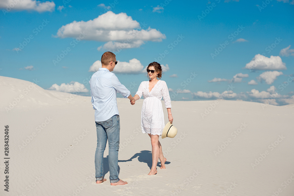 Young couple enjoying the sunset in the dunes. Romantic traveler walks in the desert. Adventure travel lifestyle concept. Young couple enjoying the sunset in the dunes. Romantic traveler walks in the desert. Adventure travel lifestyle concept.