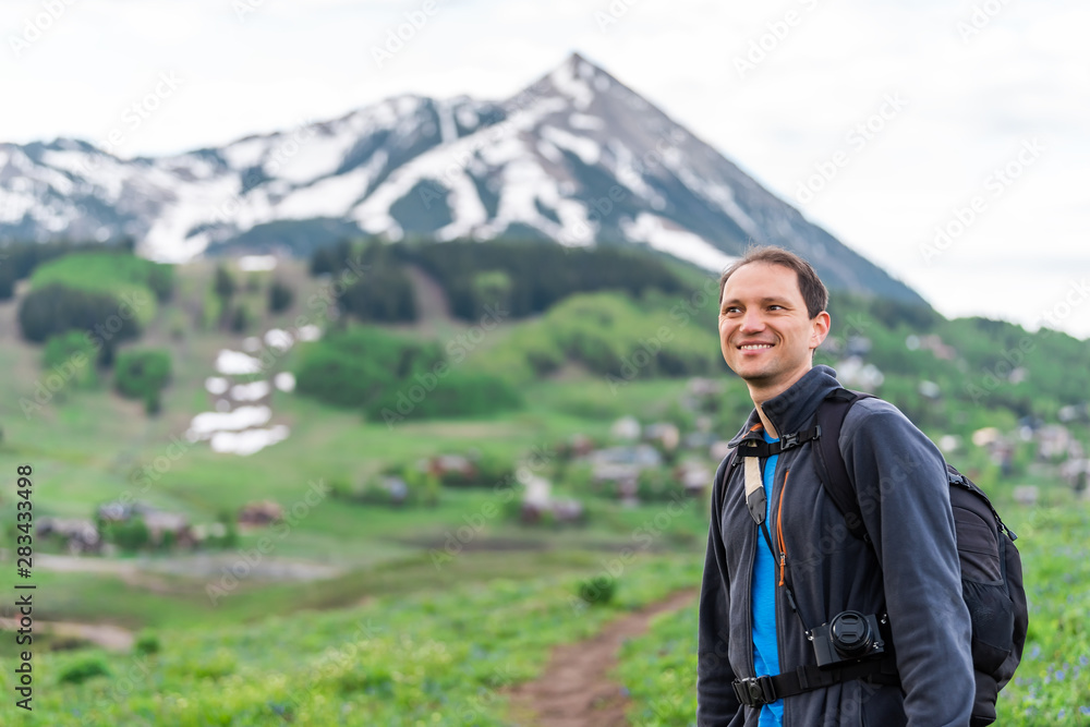 Man happy hiking closeup of face on Snodgrass trail with bokeh background view of Mount Crested Butte, Colorado peak and village in summer Man happy hiking closeup of face on Snodgrass trail with bokeh background view of Mount Crested Butte, Colorado peak and village in summer