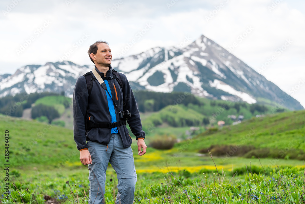 Man standing on Snodgrass trail with camera and bokeh background view of Mount Crested Butte, Colorado peak and village in summer