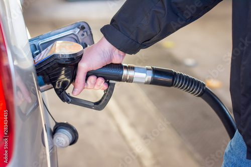 A man in a blue jeans and black coat holding pump filling gasoline. Pumping petrol into the tank. A car refuel on gas station