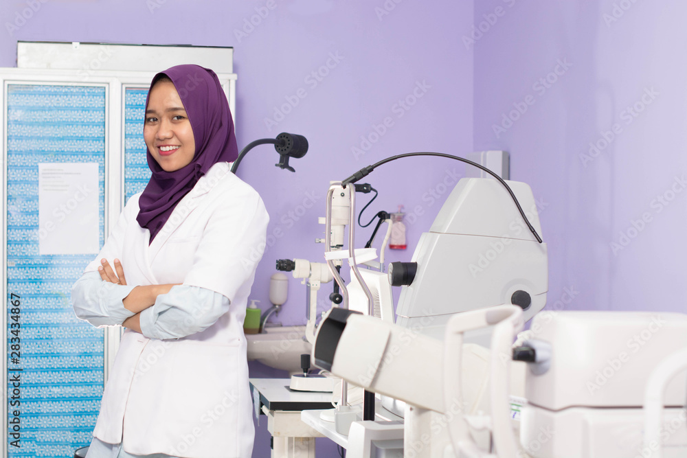 Fototapeta premium Attractive Female muslim Hijab Ophthalmologist doing eye examination to her male patient with digital Tonometer inside her clinic