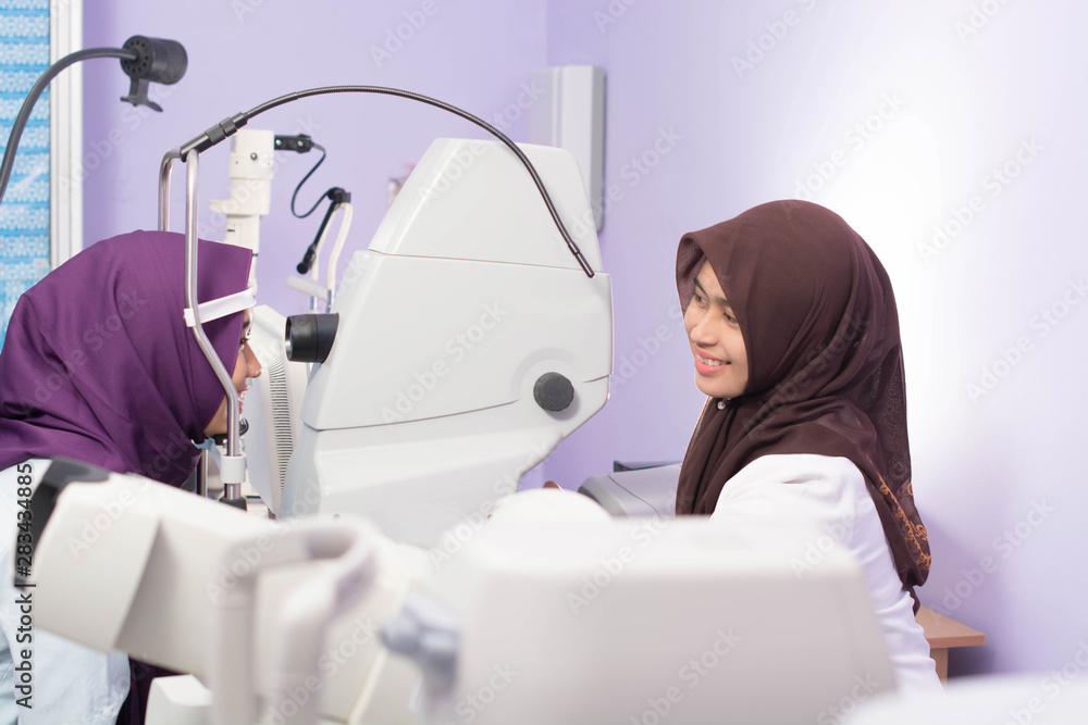 Female muslim  Hijab Ophthalmologist doing eye examination to her female hijab patient with digital Tonometer inside her clinic
