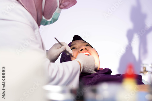 female muslim hijab dentist with her patient on dental chair doing full examination on the teeth