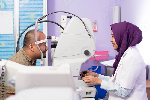 Female muslim Hijab Ophthalmologist doing eye examination to her male patient with digital Tonometer inside her clinic