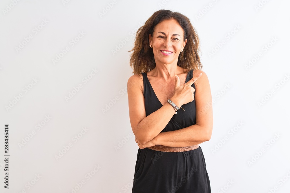 Middle age woman wearing black casual dress standing over isolated white background cheerful with a smile of face pointing with hand and finger up to the side with happy and natural expression on face Middle age woman wearing black casual dress standing over isolated white background cheerful with a smile of face pointing with hand and finger up to the side with happy and natural expression on face
