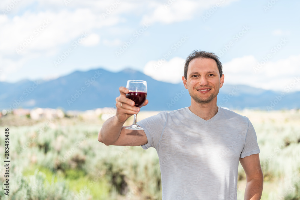 Man toasting red wine by view of Taos Sangre de Cristo mountains view from Ranchos de Taos valley bokeh background in backyard Man toasting red wine by view of Taos Sangre de Cristo mountains view from Ranchos de Taos valley bokeh background in backyard