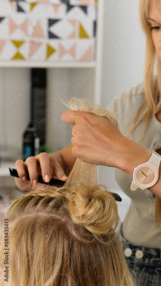 Naklejka premium Hairtician builds upper bun. Hairstyle on bob. Hairdressing services. Creating evening hairstyles fashionable stylish women's hairstyles. Process of hair styling. Courses in hairdressing. Beauty salon