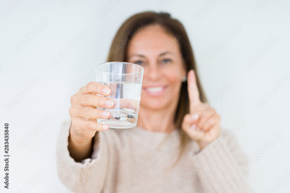 Middle age woman drinking glass of water isolated background surprised with an idea or question pointing finger with happy face, number one Middle age woman drinking glass of water isolated background surprised with an idea or question pointing finger with happy face, number one