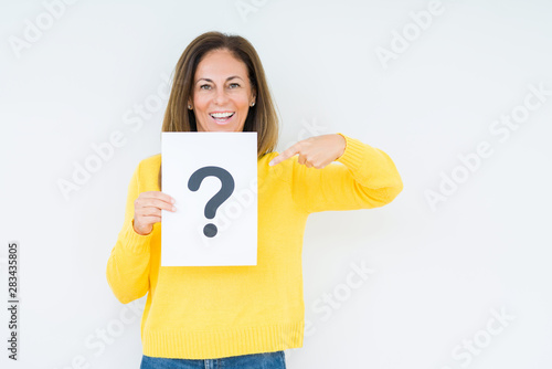 Middle age woman thinking and holding paper with question mark symbol over isolated background very happy pointing with hand and finger