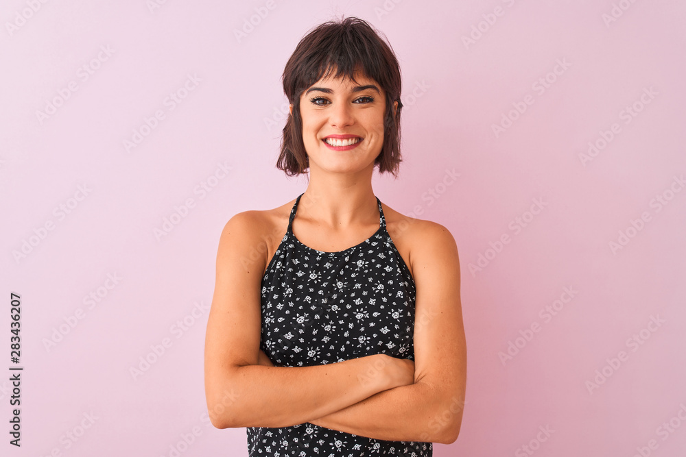 Young beautiful woman wearing black floral dress standing over isolated pink background happy face smiling with crossed arms looking at the camera. Positive person. Young beautiful woman wearing black floral dress standing over isolated pink background happy face smiling with crossed arms looking at the camera. Positive person.
