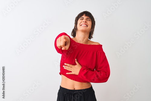 Young beautiful woman wearing red summer t-shirt standing over isolated white background laughing at you, pointing finger to the camera with hand over body, shame expression