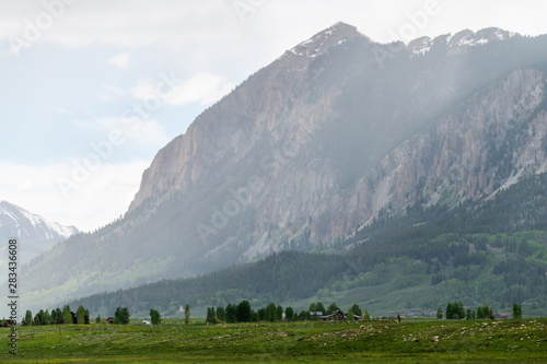Mount Crested Butte village in summer with sun rays or rain and mountain cliff with alpine meadows in early summer