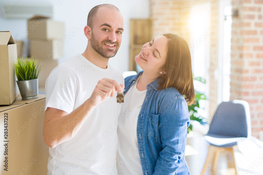 Fototapeta premium Young couple smiling very happy showing keys of new home, moving and buying new apartmet concept