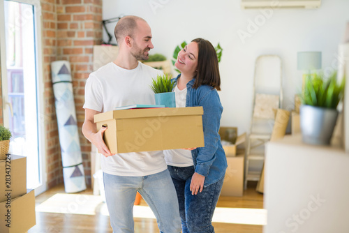 Young couple moving to a new home, smiling happy holding cardboard boxes