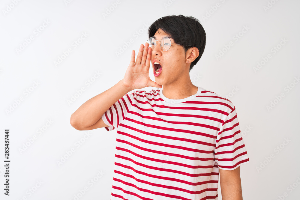 Young chinese man wearing glasses and striped t-shirt standing over isolated white background shouting and screaming loud to side with hand on mouth. Communication concept. Young chinese man wearing glasses and striped t-shirt standing over isolated white background shouting and screaming loud to side with hand on mouth. Communication concept.