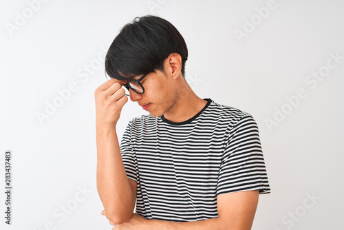 Chinese man wearing glasses and navy striped t-shirt standing over isolated white background tired rubbing nose and eyes feeling fatigue and headache. Stress and frustration concept.