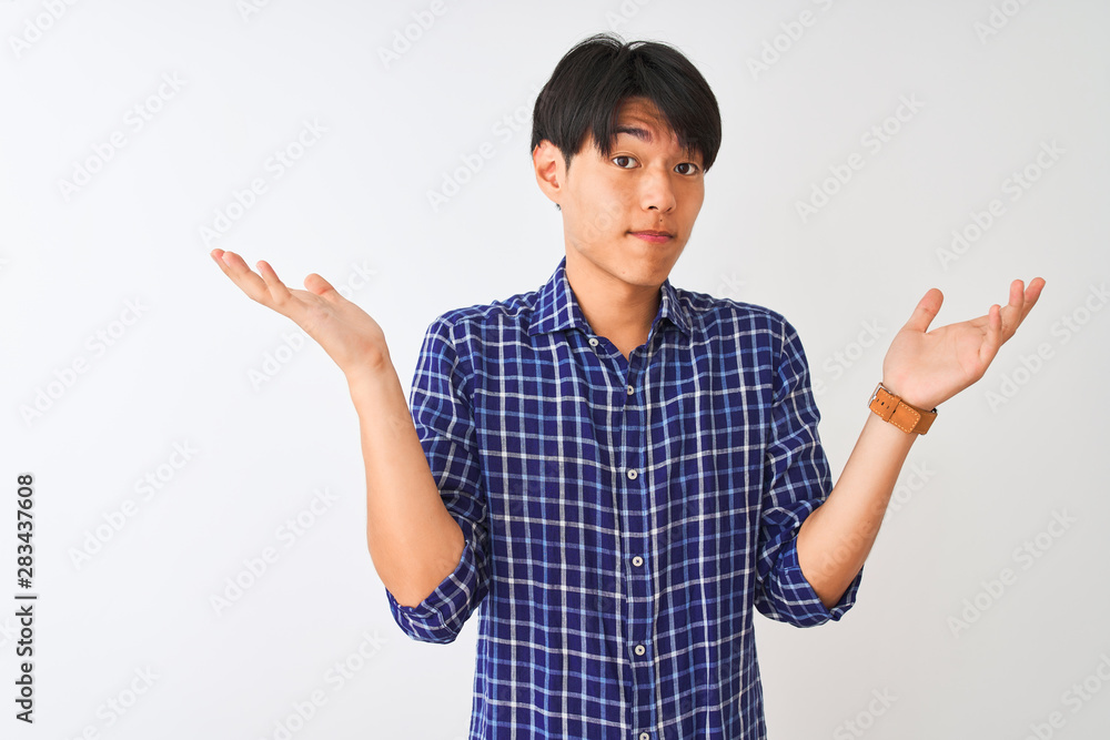 Young chinese man wearing casual blue shirt standing over isolated white background clueless and confused expression with arms and hands raised. Doubt concept. Young chinese man wearing casual blue shirt standing over isolated white background clueless and confused expression with arms and hands raised. Doubt concept.