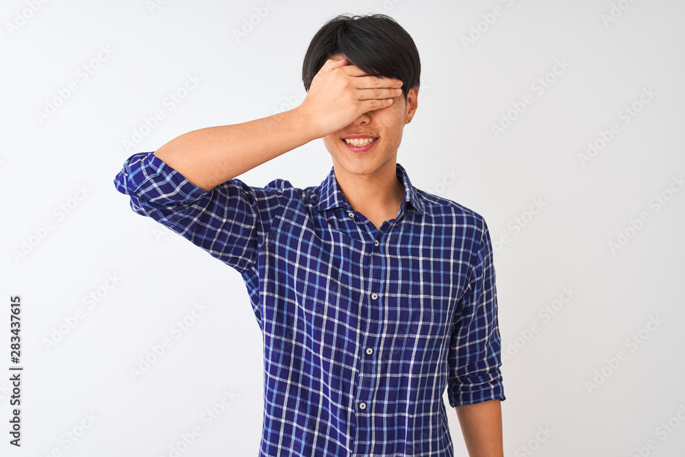 Young chinese man wearing casual blue shirt standing over isolated white background smiling and laughing with hand on face covering eyes for surprise. Blind concept.