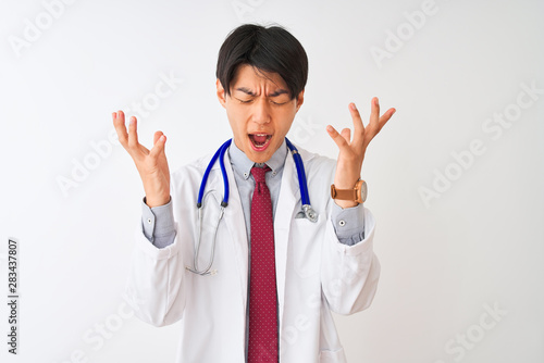 Chinese doctor man wearing coat tie and stethoscope over isolated white background celebrating mad and crazy for success with arms raised and closed eyes screaming excited. Winner concept