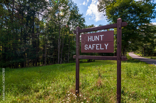 A wooden sign saying HUNT SAFELY on the side of a road in Warren county, Pennsylvania, USA on a sunny, summer day