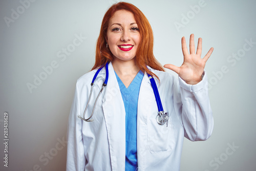 Young redhead doctor woman using stethoscope over white isolated background showing and pointing up with fingers number five while smiling confident and happy.