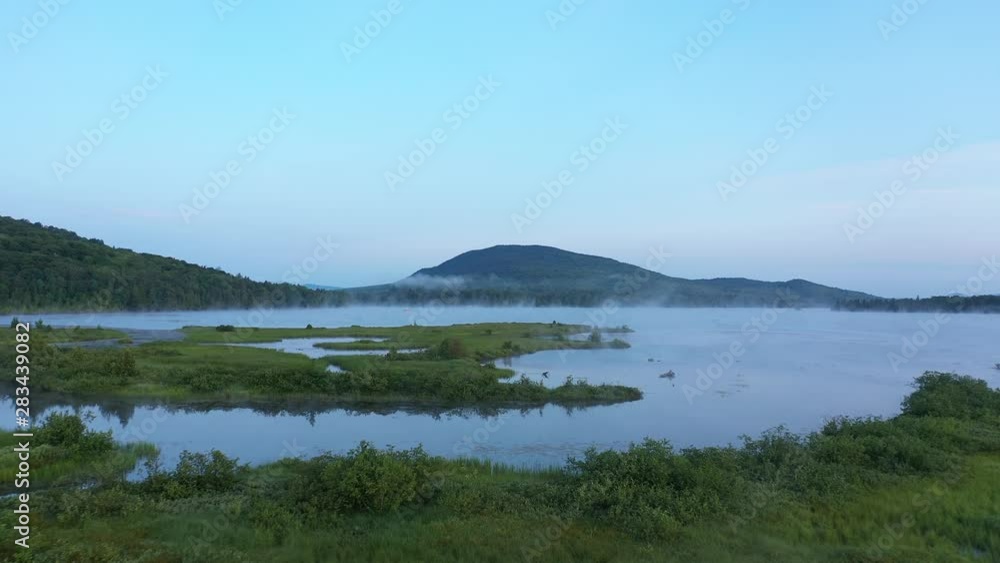 Wide aerial sunrise shot over grass and blue water under mountain peak. Wide aerial sunrise shot over grass and blue water under mountain peak.
