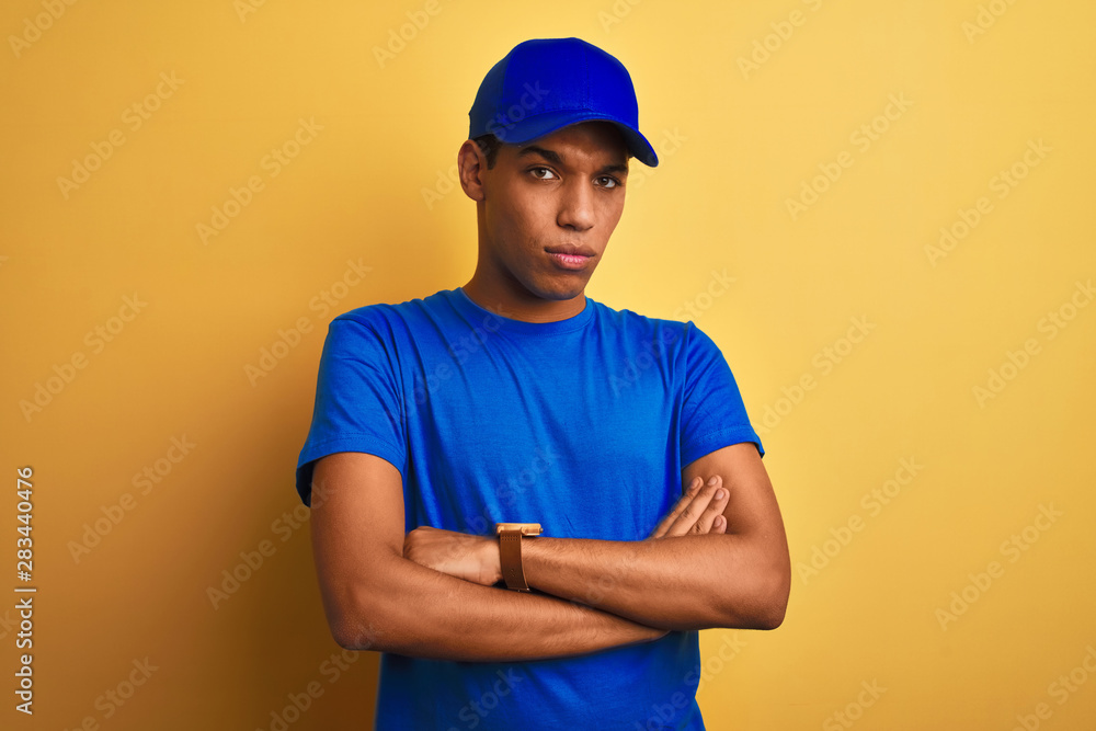 Young handsome arab delivery man standing over isolated yellow background skeptic and nervous, disapproving expression on face with crossed arms. Negative person.