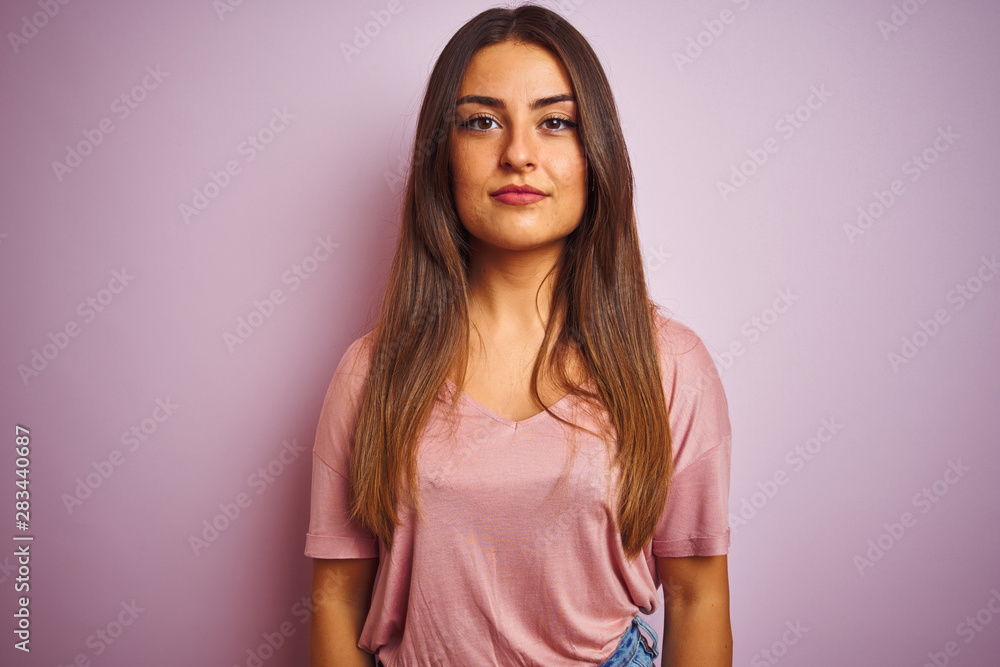 Young beautiful woman wearing t-shirt standing over isolated pink background with serious expression on face. Simple and natural looking at the camera. Young beautiful woman wearing t-shirt standing over isolated pink background with serious expression on face. Simple and natural looking at the camera.