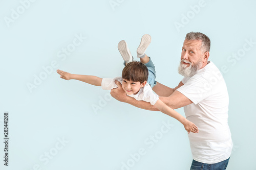 Cute little boy playing with grandfather on light background